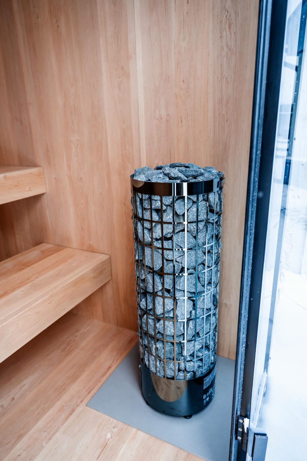 Warm OneEighty sauna interior with timber benches and a stone heater