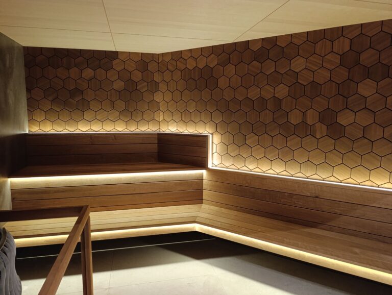 Hotel sauna with walnut-toned hexagon wall panels above lit timber benches