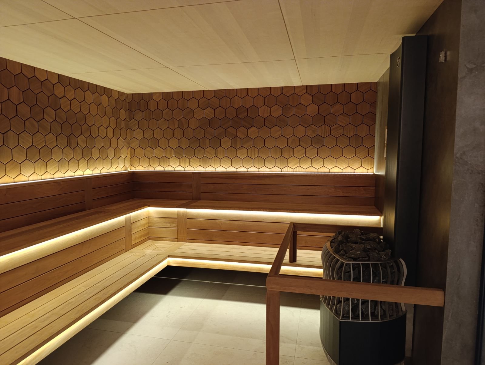 Hexagon-panelled hotel sauna with the stone heater and a timber handrail