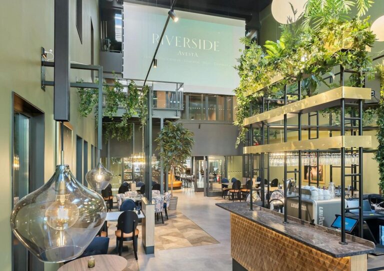 Hotel bar counter clad in faceted wood panels under hanging greenery