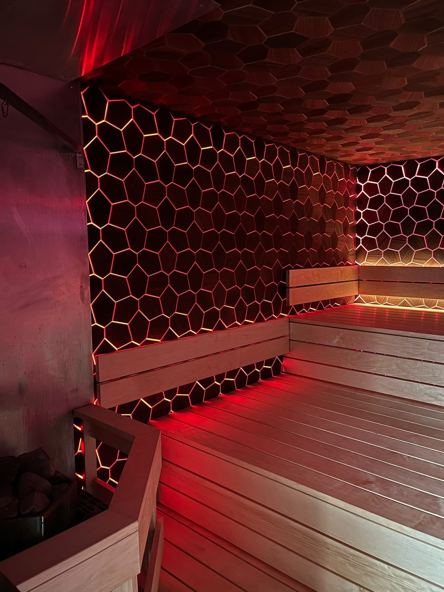 Sauna lined in EmotionWood hexagon panels with the built-in lighting set to red